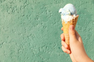 Photo of Woman holding delicious ice cream in wafer cone near turquoise wall, closeup. Space for text