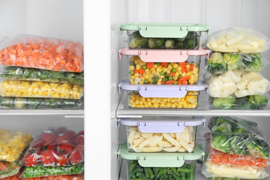 Plastic bags and containers with different frozen vegetables in refrigerator