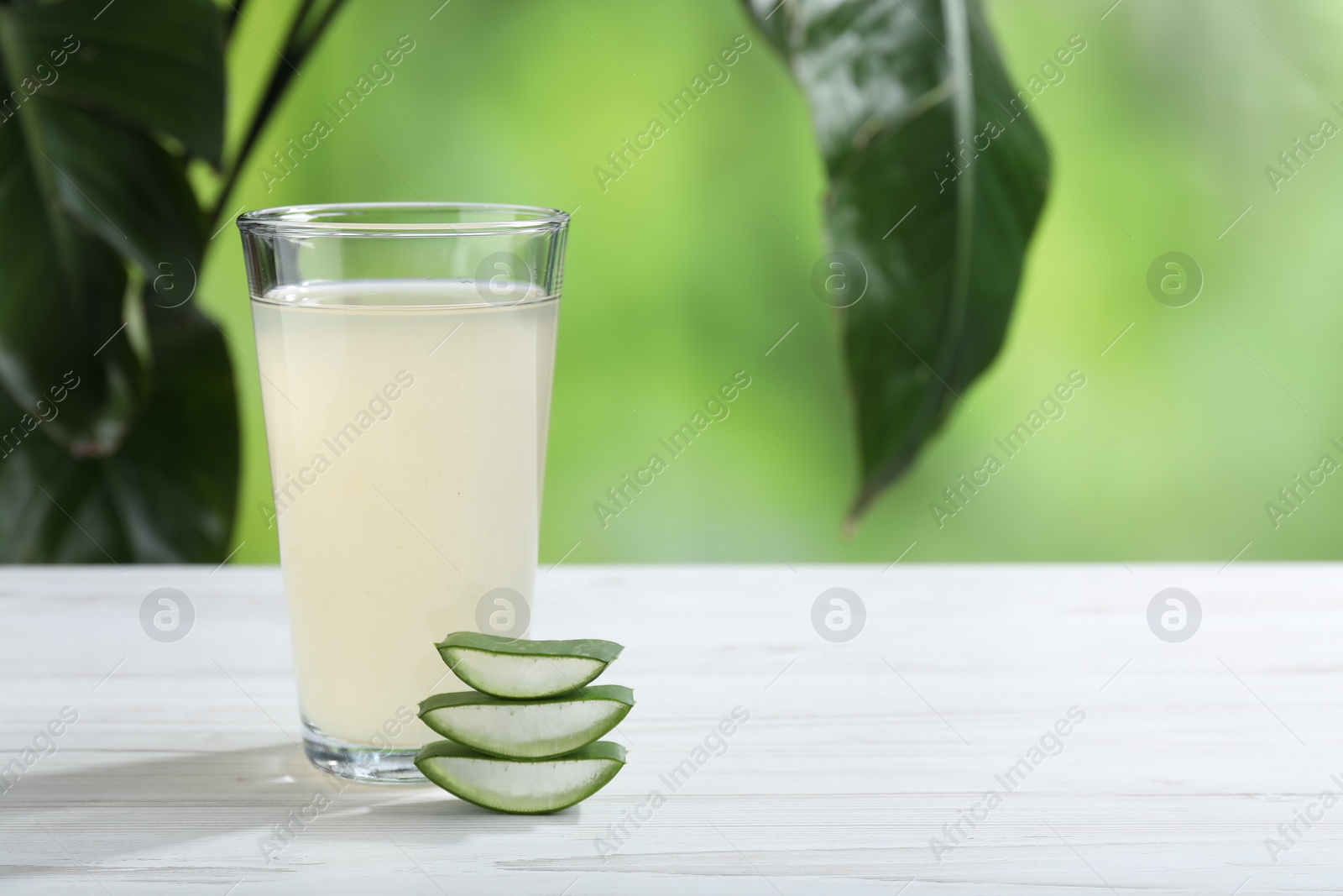 Photo of Fresh aloe juice in glass and cut leaves on white wooden table outdoors, space for text