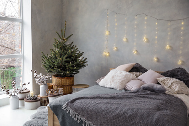 Photo of Little Christmas tree with fairy lights in bedroom interior