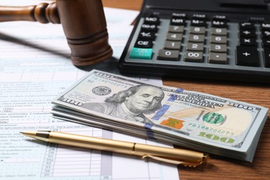 Tax return form, dollar banknotes, gavel, pen and calculator on wooden table, closeup