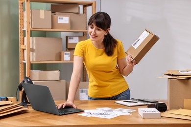 Parcel packing. Post office worker with box using laptop at wooden table indoors