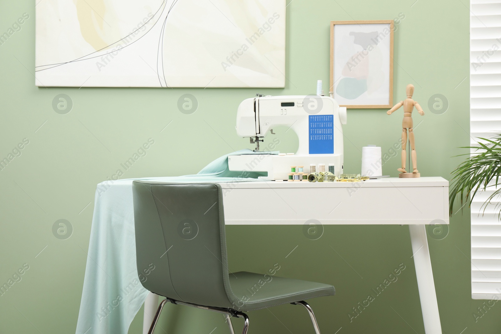 Photo of Modern sewing machine with cloth and craft accessories on white table near window in room