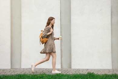 Young woman with cup of drink walking near stone wall outdoors, space for text