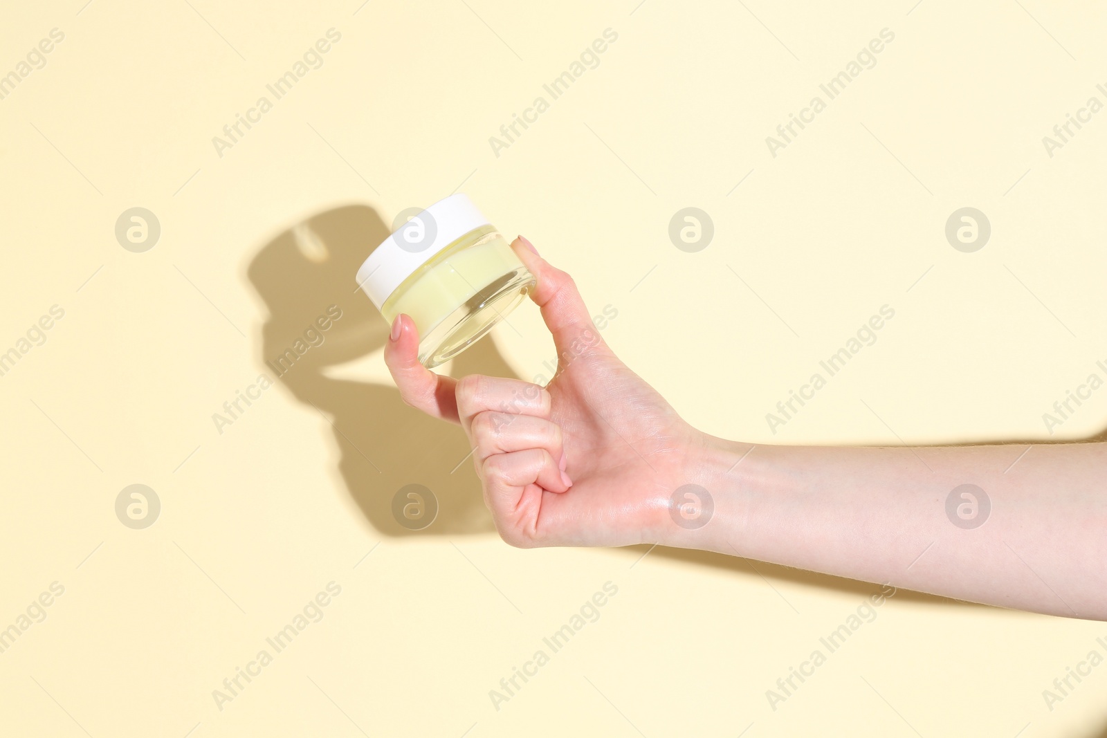 Photo of Woman holding jar of cream on yellow background, closeup