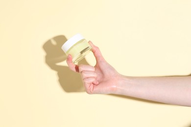 Woman holding jar of cream on yellow background, closeup