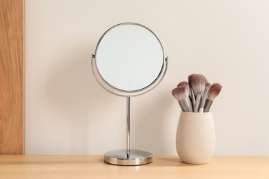 Photo of Mirror and makeup brushes on wooden dressing table in room