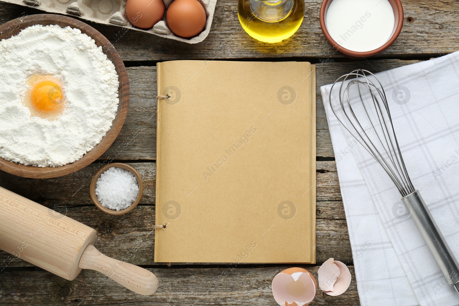 Photo of Blank recipe book surrounded by different ingredients on wooden table, flat lay. Space for text