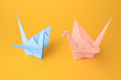 Origami art. Beautiful light blue and pale pink paper cranes on orange background
