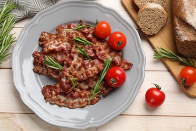 Photo of Slices of tasty fried bacon with rosemary and tomatoes served on wooden table, flat lay