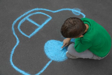 Child drawing car with chalk on asphalt