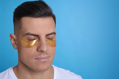 Man with golden under eye patches on light blue background. Space for text