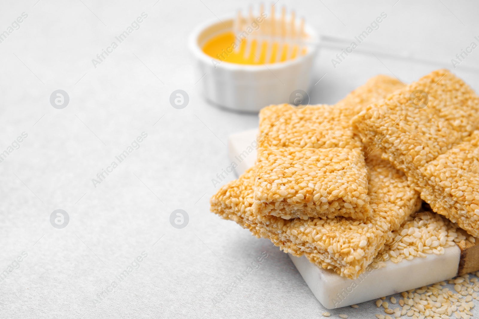 Photo of Delicious sesame kozinaki bars and honey on white table, closeup. Space for text