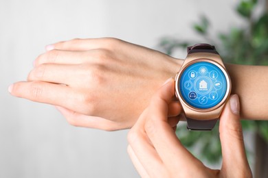 Woman setting smart home control system via smartwatch indoors, closeup. App interface with icons on display