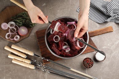 Photo of Woman stringing marinated meat on skewer at table, top view