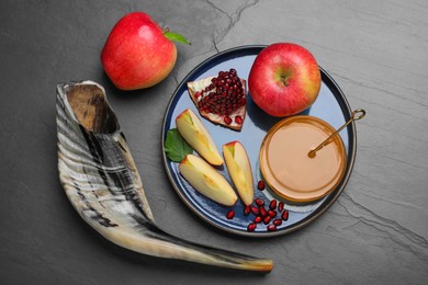 Photo of Honey, pomegranate, apples and shofar on black table, flat lay. Rosh Hashana holiday