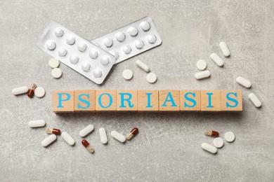 Photo of Word Psoriasis made of wooden cubes with letters and pills on light gray textured table, flat lay