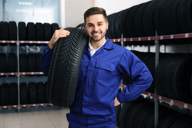 Male mechanic with car tire in auto store