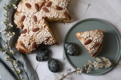 Delicious Italian Easter dove cake (traditional Colomba di Pasqua), painted eggs and branches with beautiful flowers on white marble table, flat lay