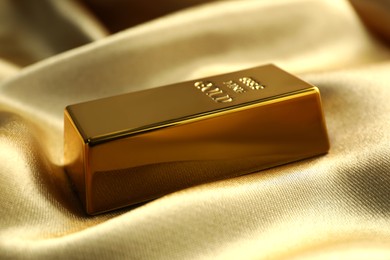 Photo of Gold bar on shiny silk fabric, closeup