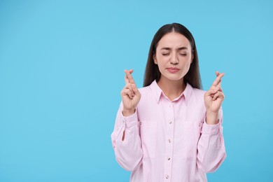 Photo of Beautiful woman crossing her fingers on light blue background, space for text