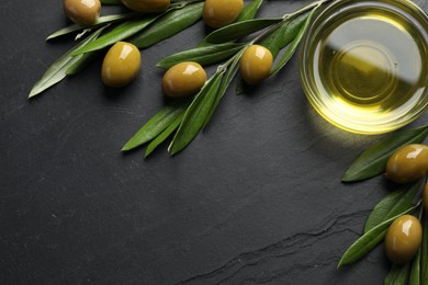 Cooking oil in bowl, olives and leaves on black textured table, flat lay. Space for text