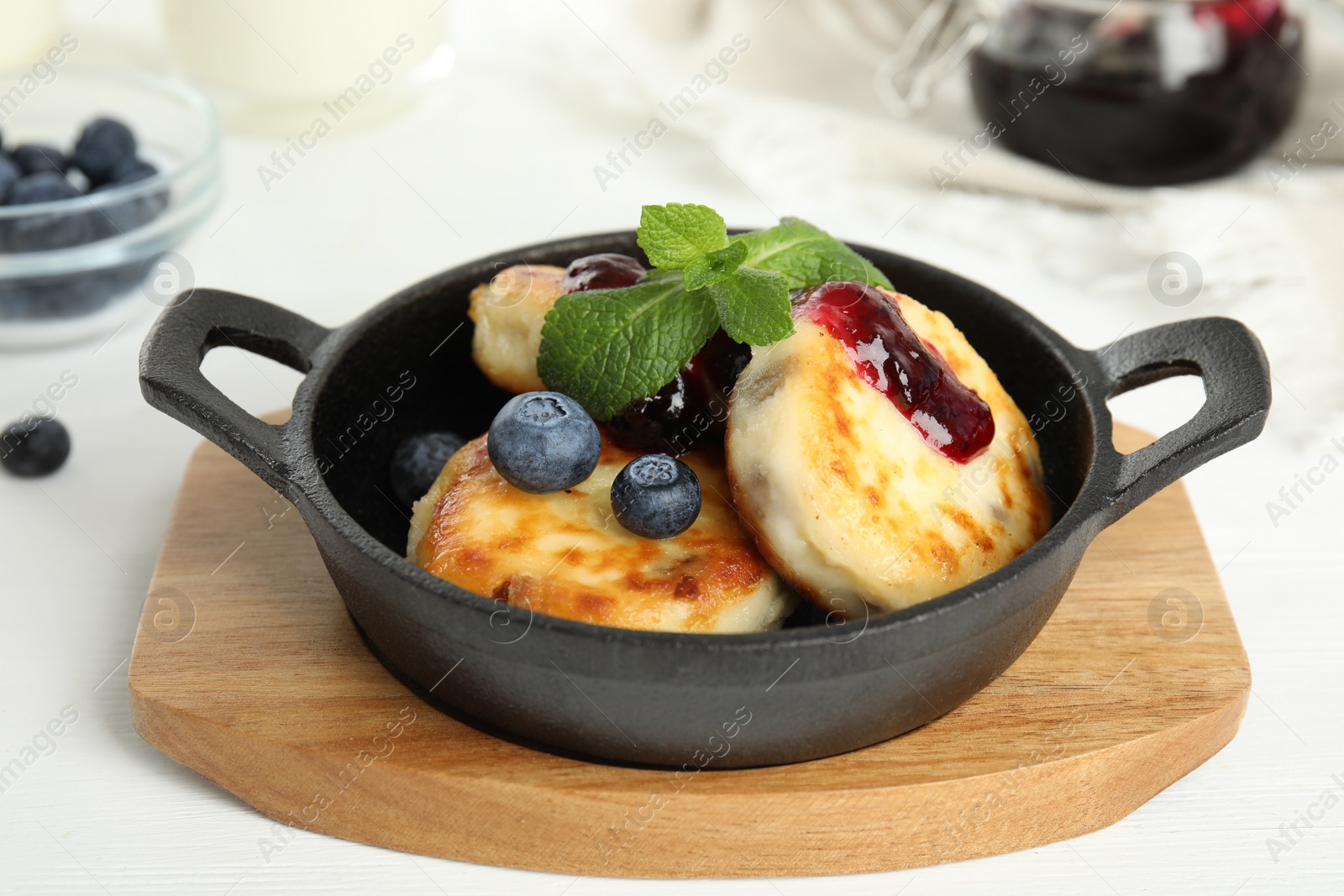 Photo of Delicious cottage cheese pancakes with blueberries, mint and jam in pan on white wooden table