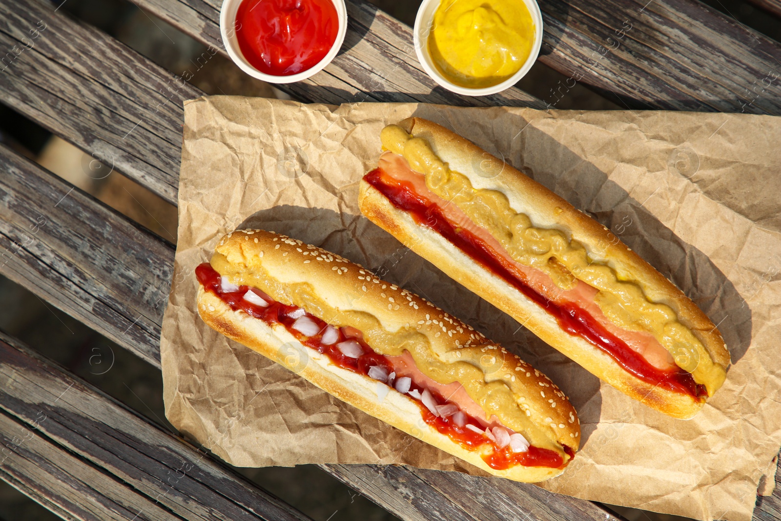 Photo of Fresh delicious hot dogs and sauces on wooden surface outdoors, flat lay