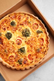 Delicious homemade vegetable quiche in carton box on light gray table, top view