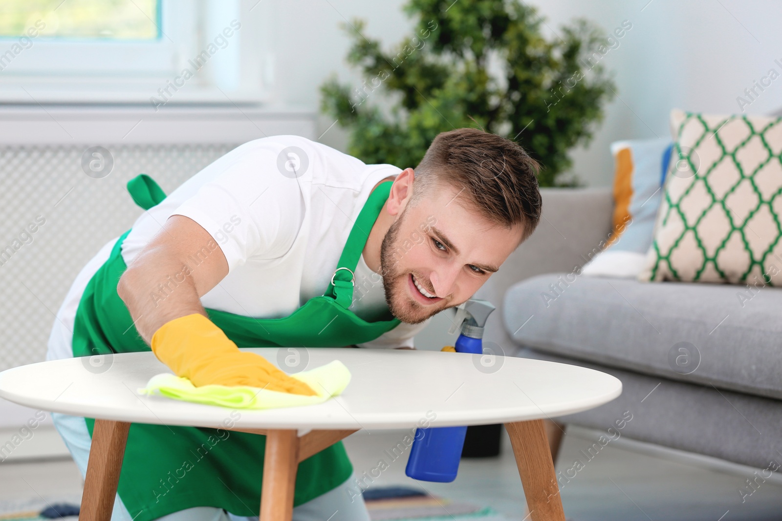 Photo of Young man cleaning table with rag indoors