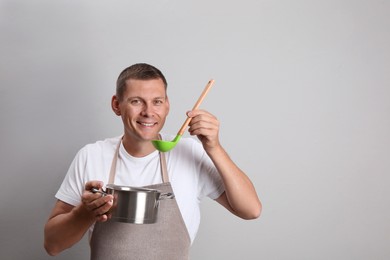 Photo of Happy man with cooking pot and ladle on light grey background. Space for text