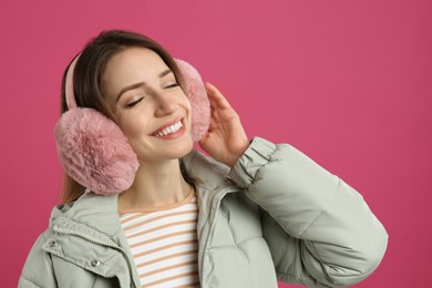 Photo of Happy woman wearing warm earmuffs on pink background