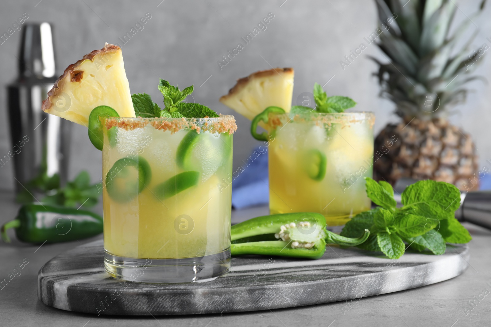 Photo of Glasses of spicy pineapple cocktail with jalapeno and mint on grey table