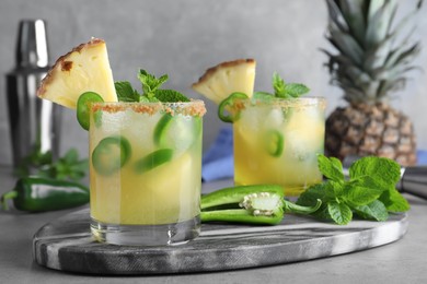 Glasses of spicy pineapple cocktail with jalapeno and mint on grey table