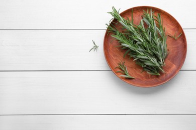 Photo of Plate with branch of fresh green rosemary on white wooden table, top view. Space for text
