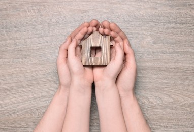 Photo of Home security concept. Woman with her little child holding house model at wooden table, top view