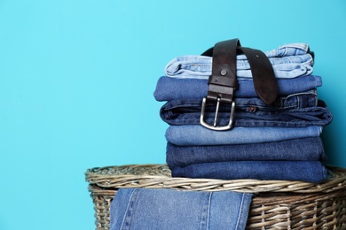 Photo of Stack of different jeans on basket against color wall with space for text