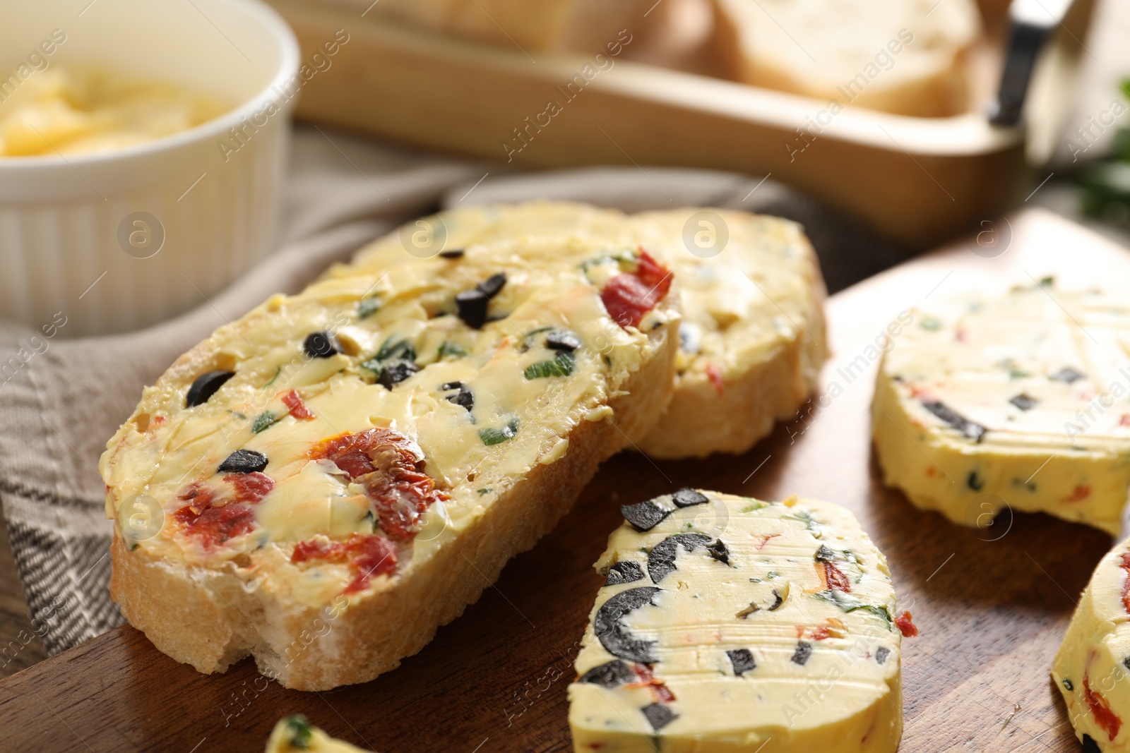 Photo of Tasty butter with olives, chili pepper, parsley and bread on table, closeup