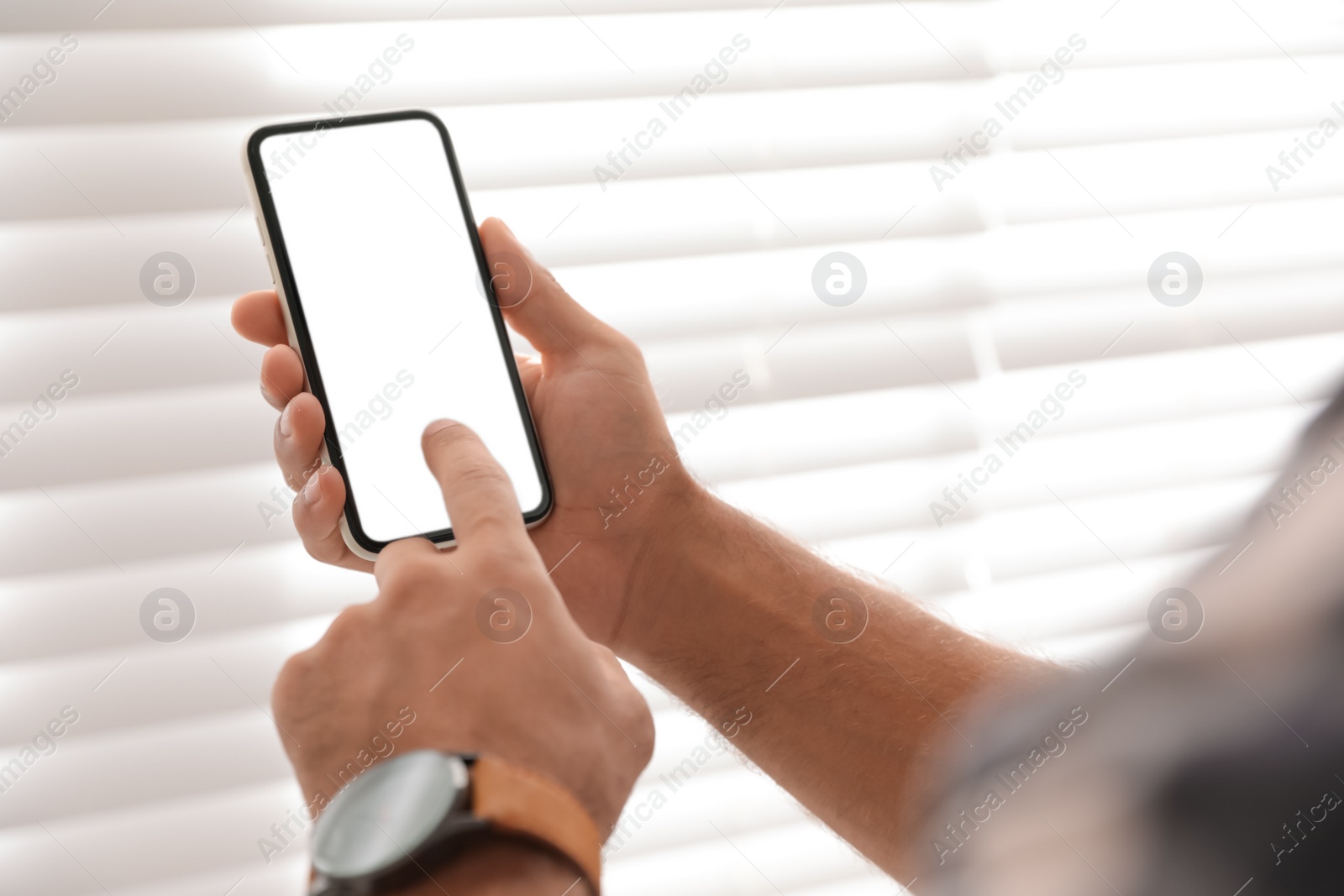 Photo of Man using mobile phone with empty screen near window indoors, closeup