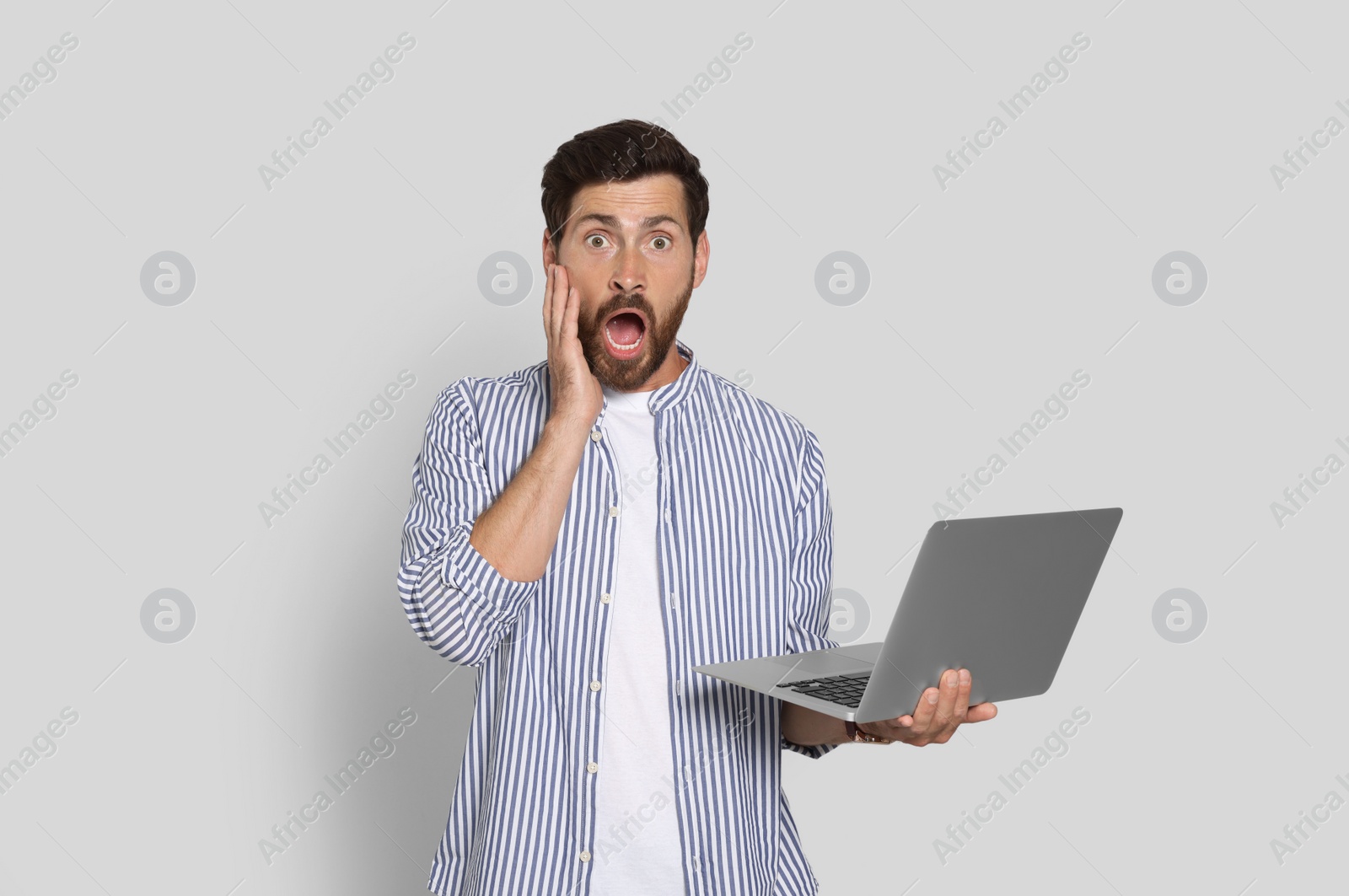 Photo of Emotional bearded man with laptop on light background