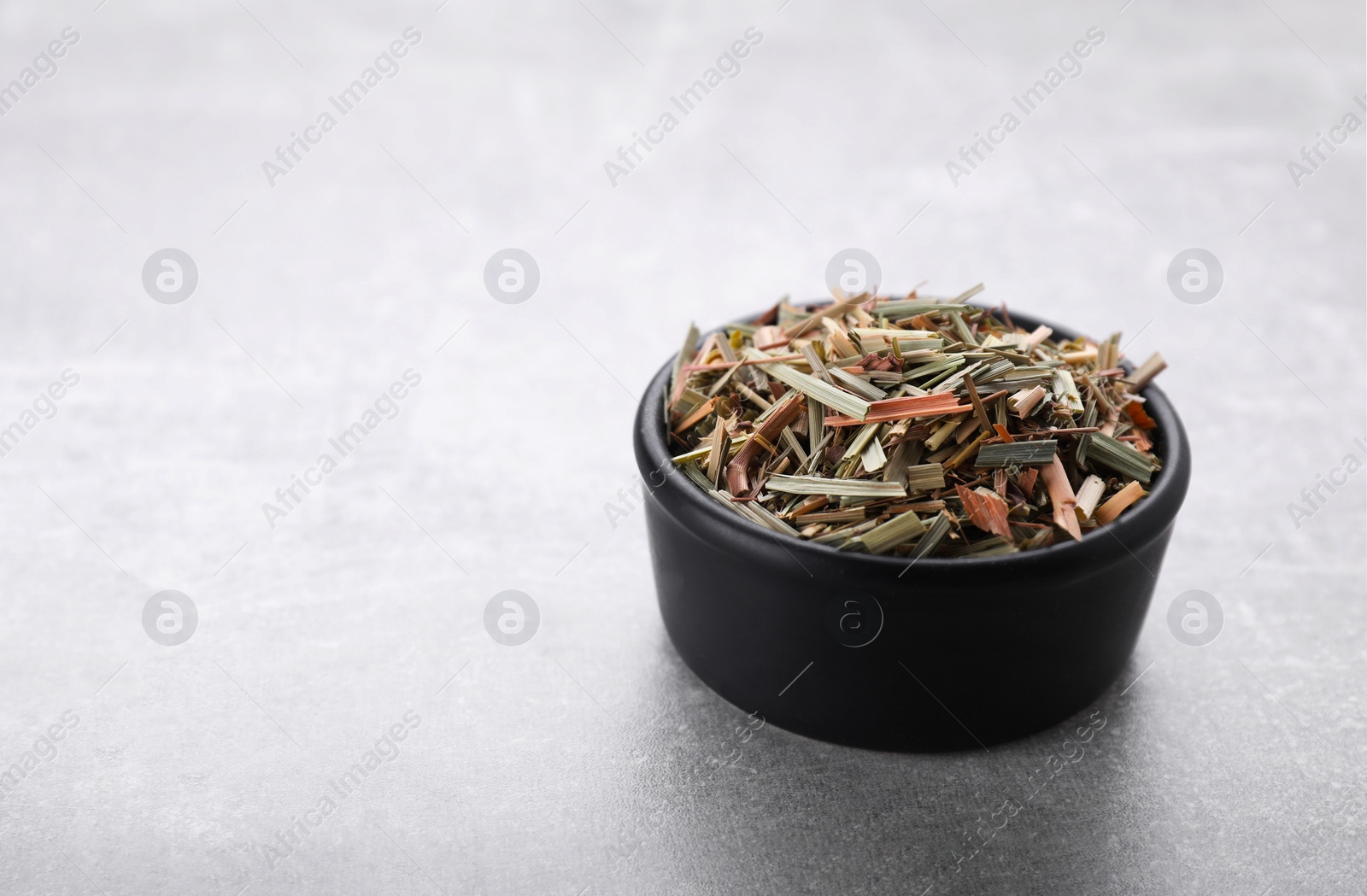 Photo of Bowl with aromatic dried lemongrass on light grey table. Space for text