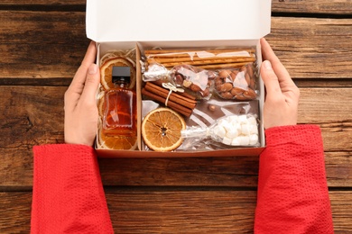 Woman holding box with stylish craft gift set at wooden table, top view