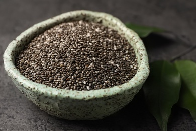Photo of Bowl with chia seeds and leaves on grey table, closeup