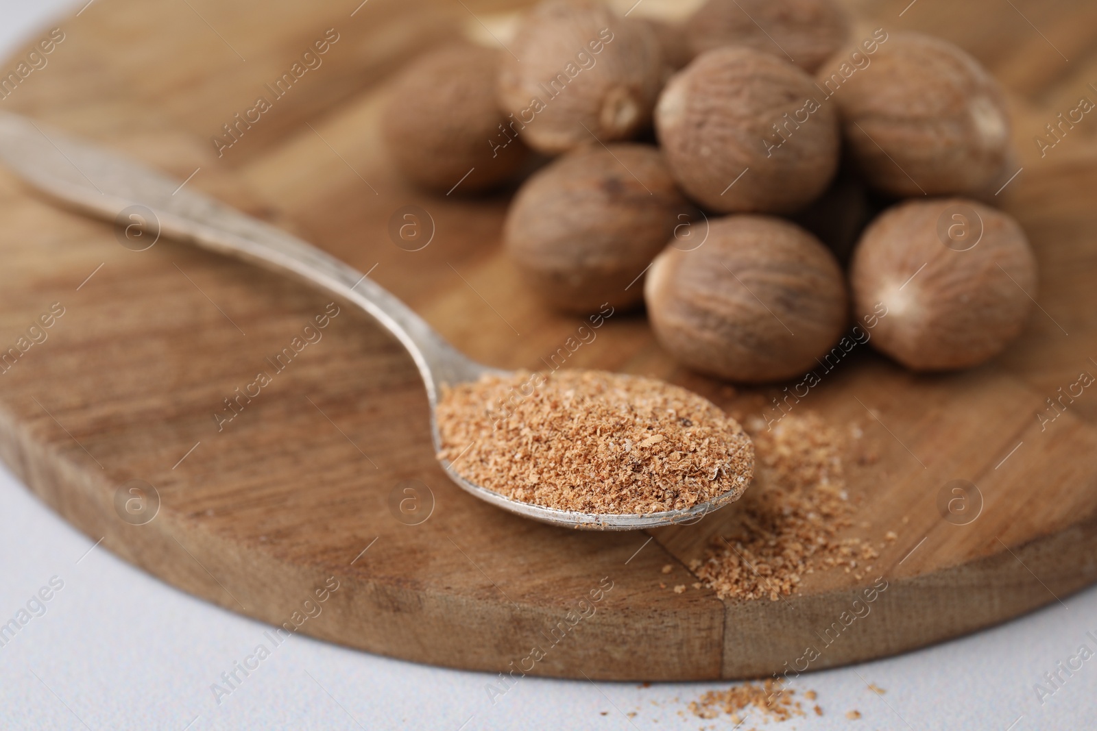 Photo of Spoon with grated nutmeg and seeds on white table, closeup