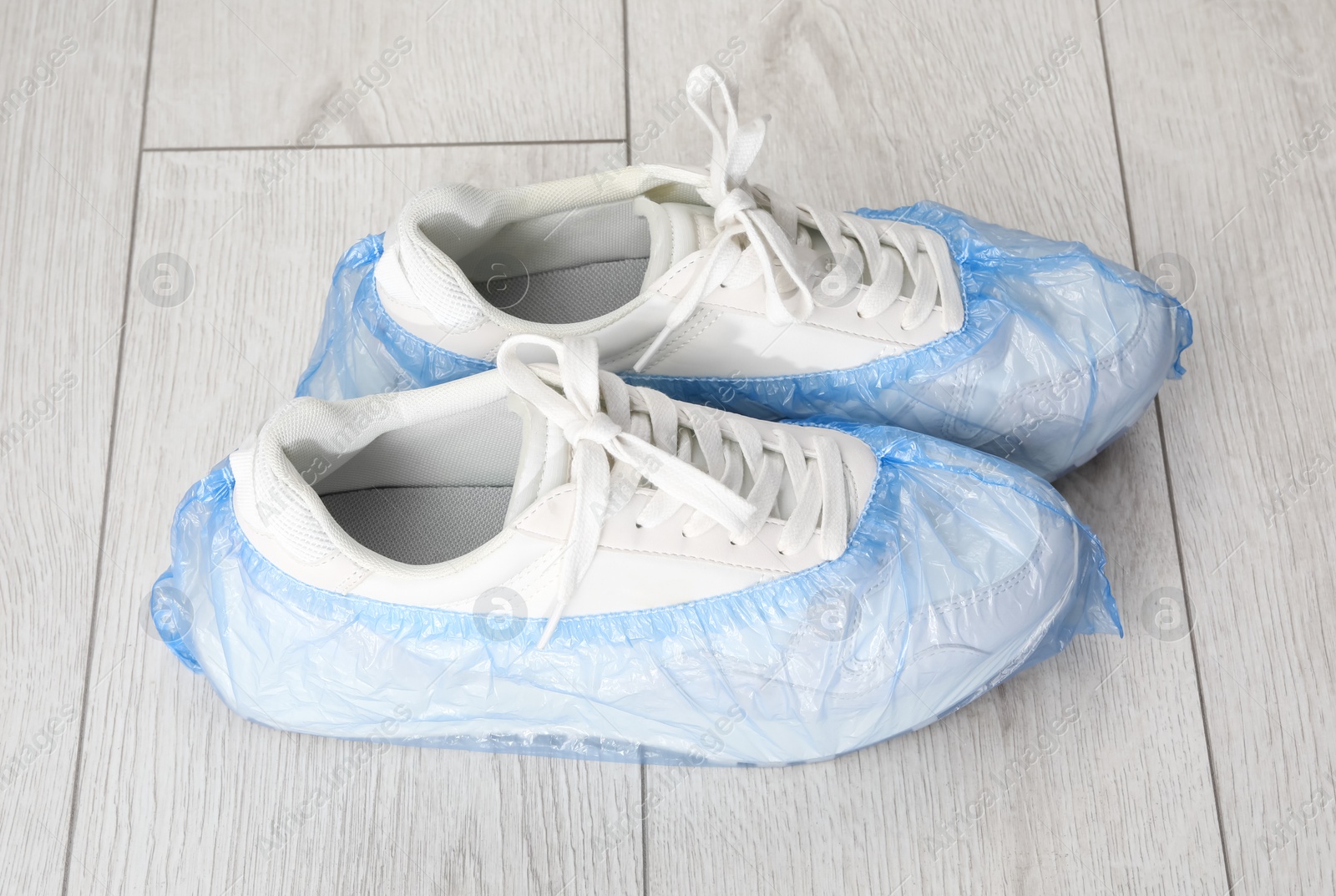 Photo of Sneakers in blue shoe covers on light wooden floor