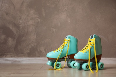 Vintage roller skates on floor near brown wall. Space for text