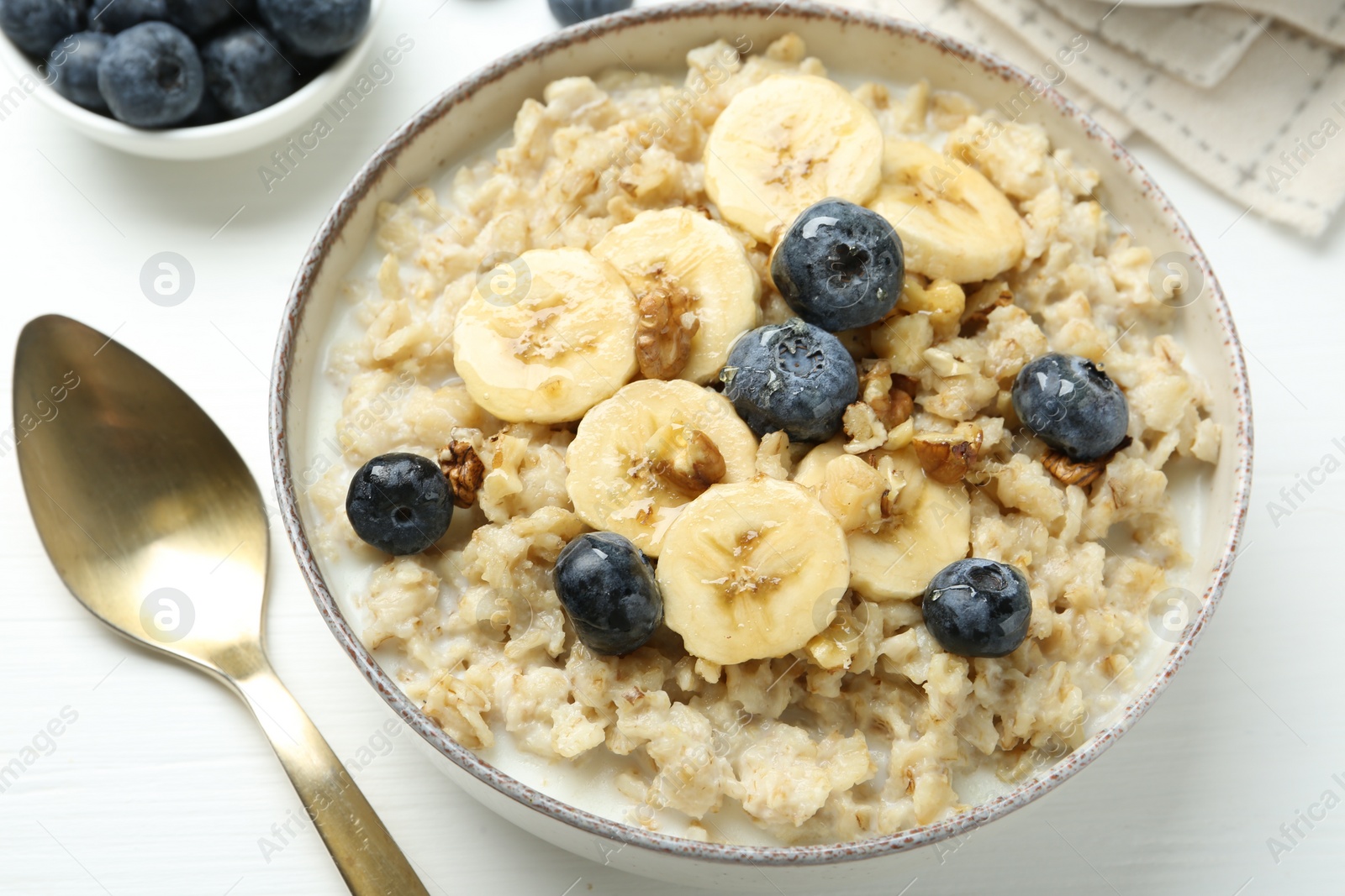 Photo of Tasty oatmeal with banana, blueberries, walnuts and honey served in bowl on white wooden table, closeup