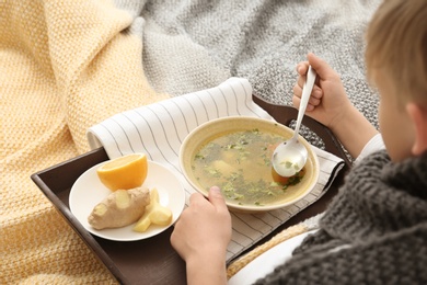 Photo of Sick little boy eating broth to cure cold in bed at home