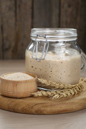 Photo of Leaven and ears of wheat on beige wooden table