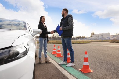 Photo of Young woman with instructor near car at driving school test track